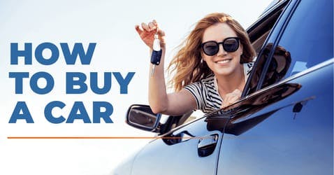 happy female driver leaning out of car window holding keys of brand-new car she just bought