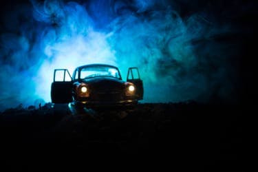 The article title over a spooky car with its doors open and headlights on, surrounded by blue smoke.