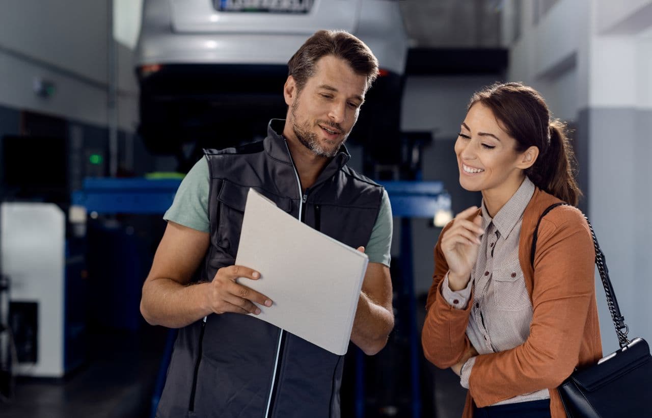 mechanic and consumer looking at MOT results with car on ramp in background