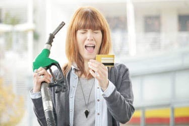 The article title over a stressed woman at a petrol station holding a petrol pump and credit card.