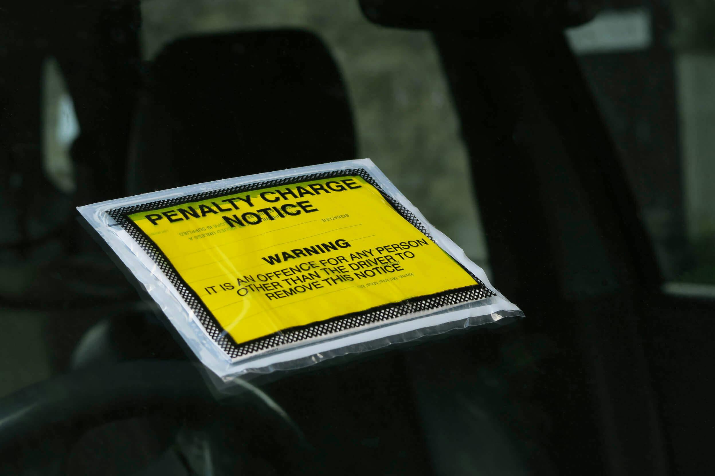 The article title over a car windscreen, with a yellow warning parking ticket taped to it.