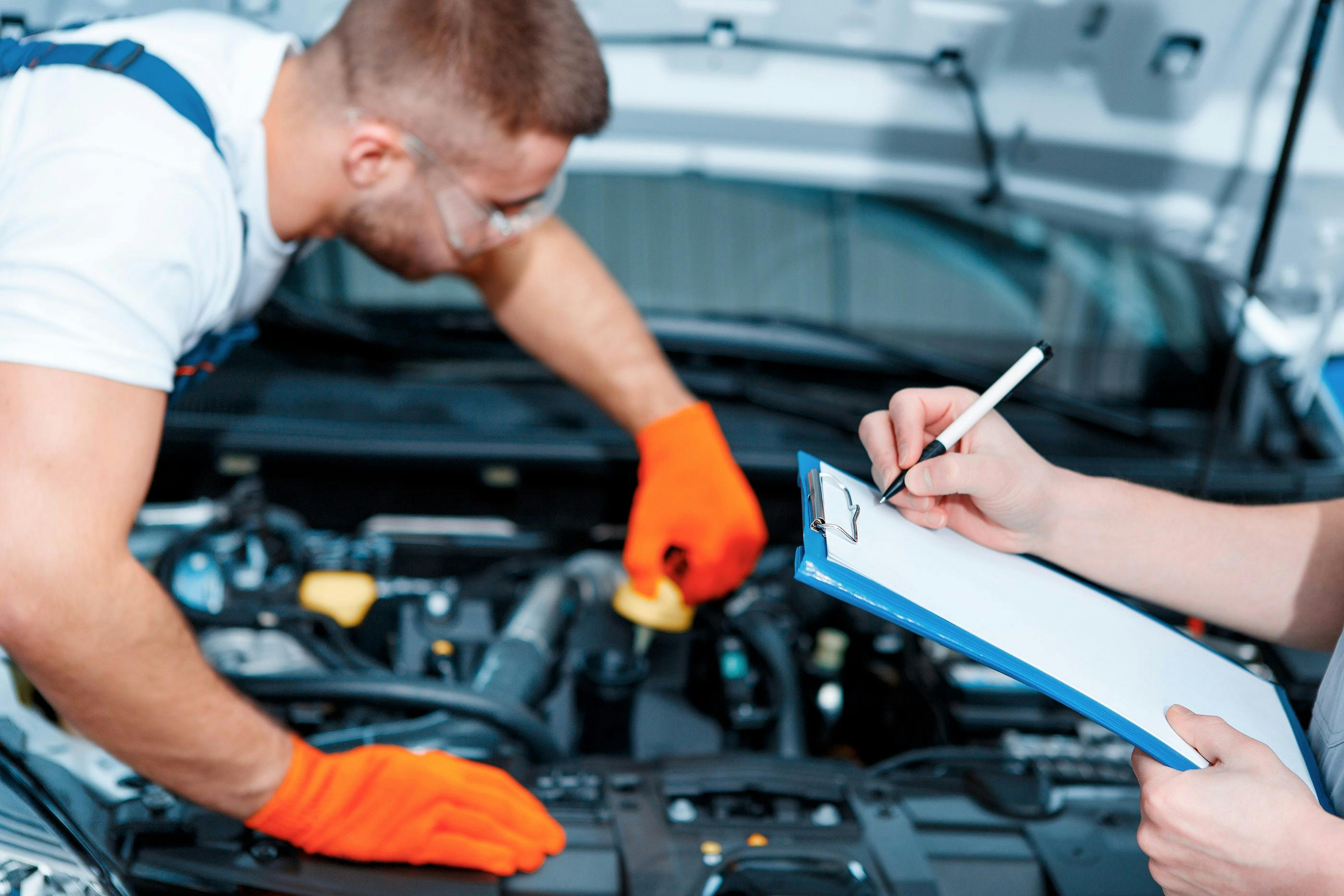 two mechanics completing car service in engine bay, one using clipboard to record results