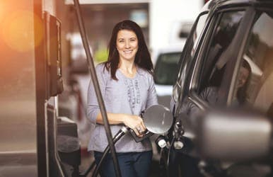 A woman with dark hair filling up her car with premium fuel at a petrol station.