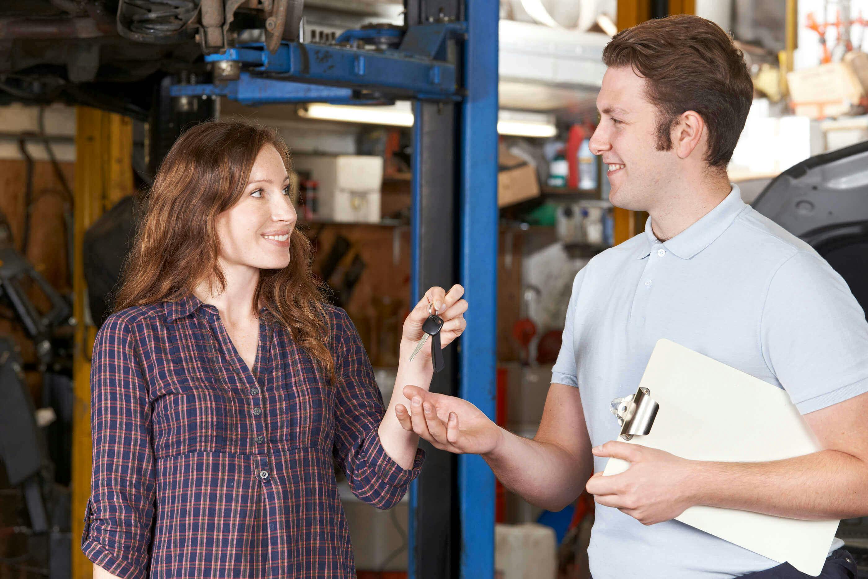 smiling female driver handing over car keys to friendly mechanic holding clipboard