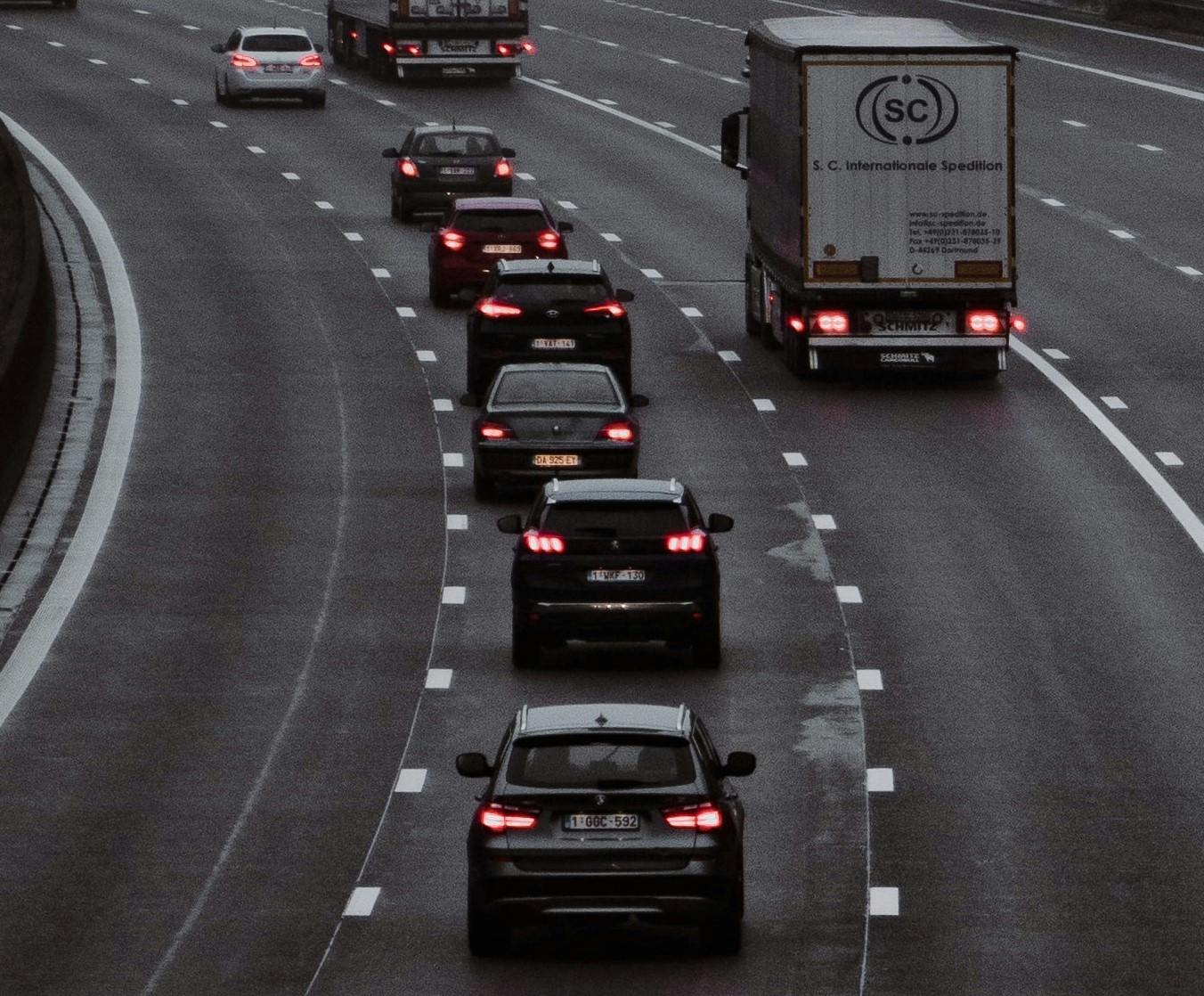 A image of a row of cars tailgating on a motorway, their brake lights illuminated red. 