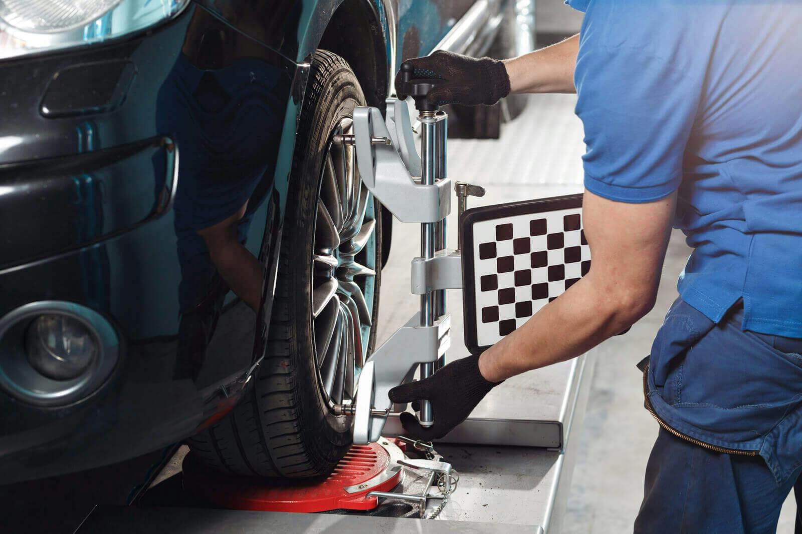 mechanic completing wheel alignment on black car in bright workshop