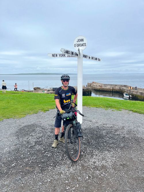 Ollie posing on his bike next to John O'Groats sign having completed his journey