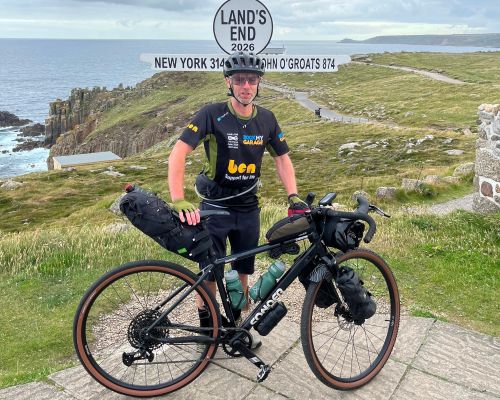 Ollie and bike stood next to Land's End sign at start of ride
